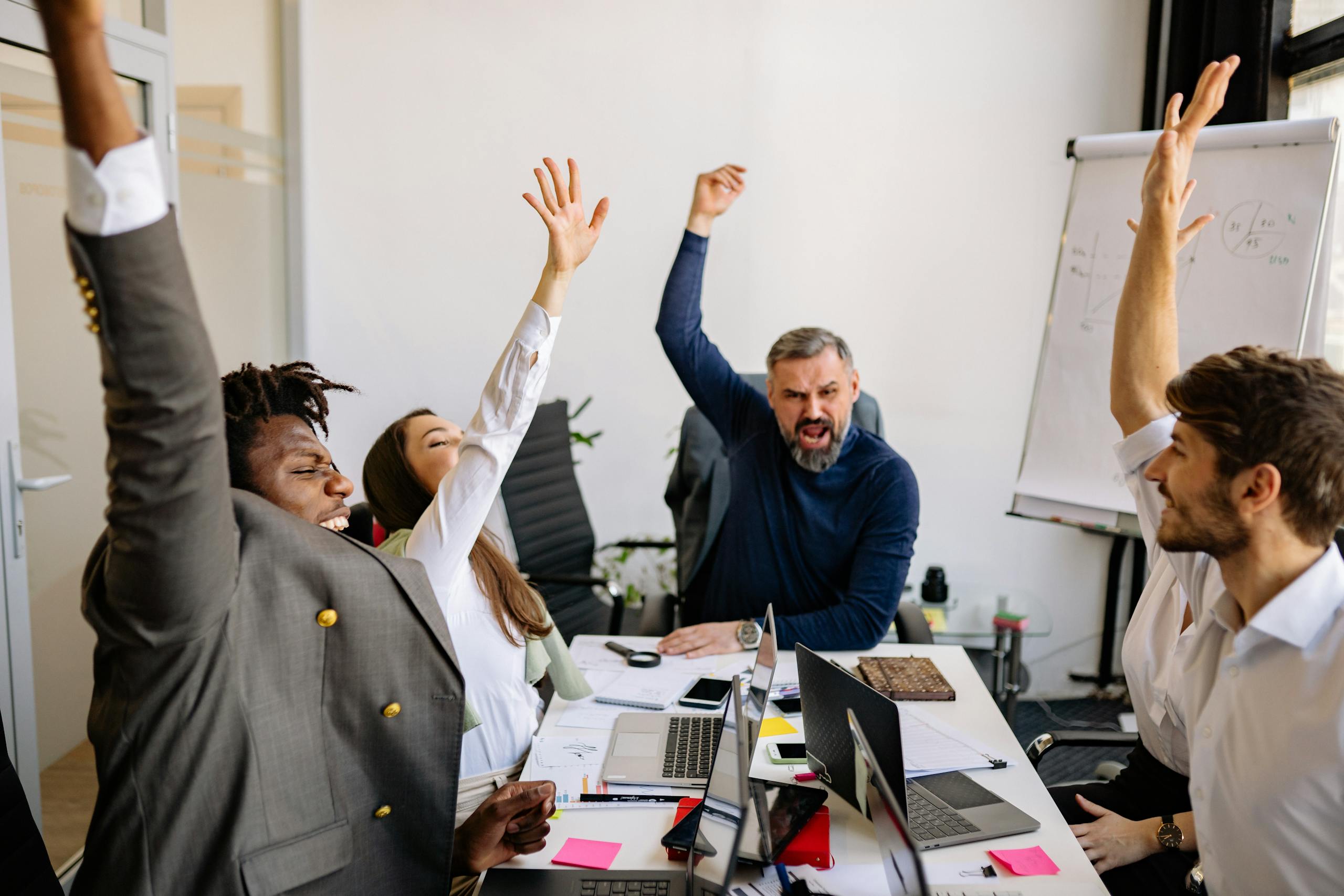 Diverse business team raising hands in excitement during a meeting in a modern office.